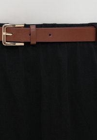 Μαύρο ύφασμα με ρυτιδωτή υφή, που διαθέτει καφέ δερμάτινη ζώνη και χρυσή μεταλλική αγκράφα. Η εστίαση βρίσκεται στο σχέδιο και την αντίθεση χρωμάτων της ζώνης.