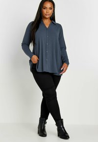 Långärmad skjorta med knappar i mörkblå ribbad tyg med krage och sidfickor, kombinerad med svarta skinny jeans och svarta ankelstövlar.