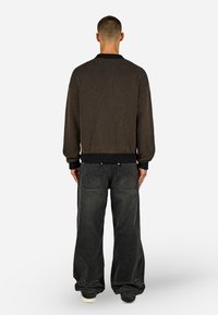 Pleteni kardigan v temno rjavi in črni črti z rebrastimi manšetami in robom, usklajen s prostimi temno sivimi kavbojkami z zadnjimi žepi.