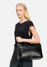 Sac à main en cuir noir au design structuré, doté de deux poignées de transport, d'une bandoulière amovible et d'accents en métal argenté.