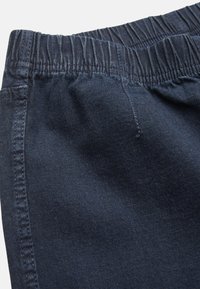 Elastische taille donkerblauwe denimstof, gladde textuur, met subtiele stikdetails. Close-up die de kwaliteit van de stof en de structuur van de tailleband toont.