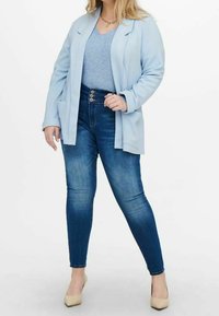 Light blue blazer over a gray top, paired with dark blue skinny jeans featuring a tall waistband and three button closure. Cream heels.
