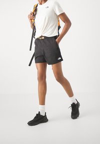 Svarta shorts med elastisk midja och sidofickor, ihop med en vit t-shirt och svarta sneakers. Ryggsäck med orange detaljer.