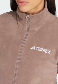 Fleece-Zip-Jacke in Hellbraun mit hohem Kragen. Mit weißem gesticktem "TERREX"-Logo und einer glatten, weichen Textur.