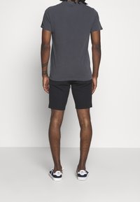 Šedé tričko s krátkým rukávem, černé šortky a námořnické tenisky s bílými podrážkami. Tričko má kulatý výstřih a volný střih.