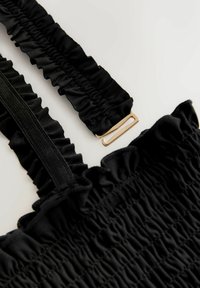 Schwarzer, gesmokter Stoff mit geraffter Struktur, ausgestattet mit einem Rüschenträger und einem goldfarbenen Metallverschluss für sicheren Halt.