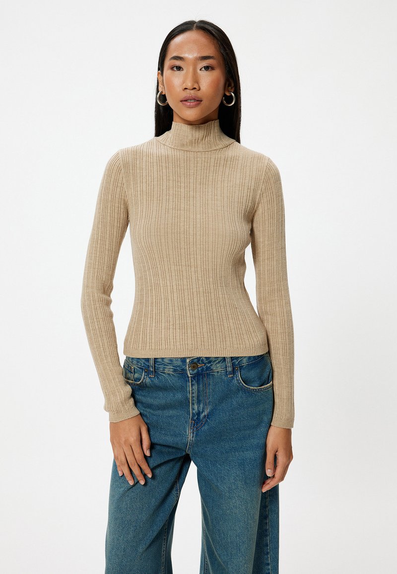 Maglione beige a collo alto con maniche lunghe, caratterizzato da una silhouette aderente. Abbinato a jeans blu a gamba larga.