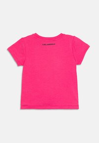 T-shirt à manches courtes et col rond en coton rose vif. Présente un logo "KARL LAGERFELD" discret en noir au dos, en haut. Texture lisse.