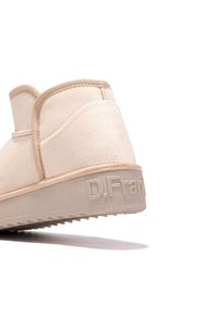 Botines de ante en color beige con suela texturizada. Presenta un acento cosido y un logo en relieve en el talón. Diseño redondeado.