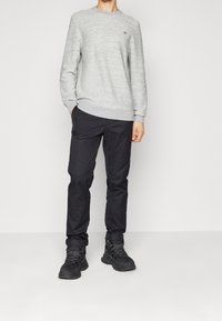 Sweatshirt gris avec une finition texturée, associé à un pantalon noir cintré et des bottes de randonnée noires avec des lacets gris. Pas de logos visibles sur le pantalon.
