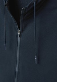 Sudadera con cremallera en color azul marino, con una textura de tela suave, cordones ajustables y una cremallera plateada. Vista cercana de la parte delantera y el forro interior.