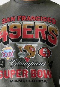 Logo der San Francisco 49ers, Football-Helme, Text zu den Super Bowl XXIX Champions und Standort Miami, Florida auf grauem Stoff.