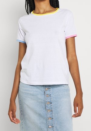 Frau trägt ein weißes Kurzarm-T-Shirt mit gelbem Kragen, blauen und pinken Ärmelsäumen, kombiniert mit einem hellblauen Jeansrock mit Knöpfen.