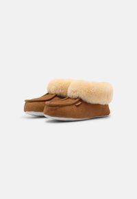 Chaussons en daim marron avec un doux revers en fourrure beige, un design à bout rond et une semelle texturée pour l'adhérence, présentant une petite étiquette sur le côté.