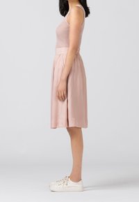 Ljusrosa satin kjol med plisseringar, kombinerad med en beige ribbad tanktop och vita sneakers. Sido- vy visar den avslappnade passformen och designen.