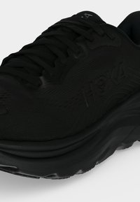 Μαύρο παπούτσι τρεξίματος Hoka με παχιά σόλα και κορδόνια, με πλαϊνή σήμανση και υφασμένο πάνω υλικό.