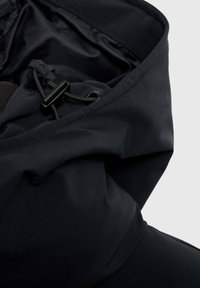 Giacca in tessuto nero con una texture liscia, cordoncino regolabile e design con colletto alto, focalizzata sulla funzionalità e resistenza alle intemperie.
