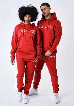 Set di felpa rossa con cappuccio e pantaloni jogger, realizzato in materiale morbido. Presenta una tasca a marsupio frontale e un logo bianco. Indossato con sneakers bianche.