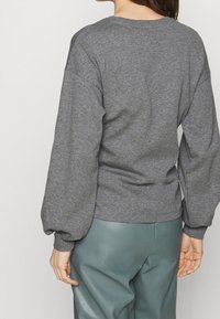 Maglione grigio con una vestibilità rilassata, caratterizzato da maniche lunghe e voluminose e un collo a coste, abbinato a pantaloni in pelle verde.