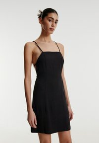 Schwarzes Kleid aus leichtem Stoff, mit einem eng anliegenden Oberteil, dünnen verstellbaren Trägern und einer geraden Silhouette, die oberhalb des Knies endet.
