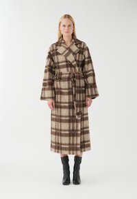 Bruin en beige geruite lange jas met een wikkeldesign, brede mouwen en een riem. Gekocht met kniehoge zwarte laarzen. Zachte, gestructureerde stof.