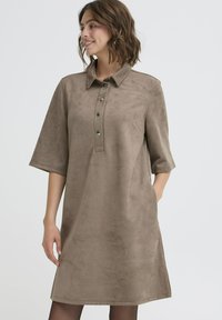 Brązowa sukienka z zamszu z kołnierzykiem, krótkimi rękawami i pięcioma guzikami z przodu. Miękka tekstura i luźny, lekko rozszerzający się krój.
