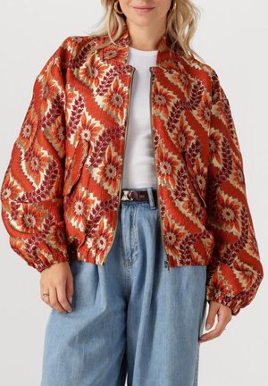 Getextureerde bomberjack in rood met bloemenpatroon; heeft een ritsclosure, geplooide mouwen en twee zijzakken. Gestyled met lichtblauwe denim.