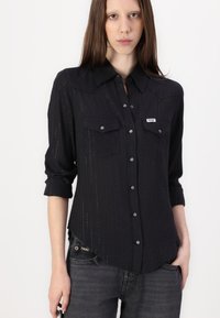 Black button-up shirt with a textured pattern, featuring a pointed collar, two chest pockets, and silver button accents.
