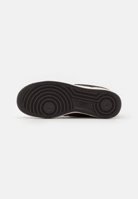 Suela de goma negra con patrón de tread circular, que cuenta con un talón reforzado y surcos de flexión para tracción y flexibilidad.