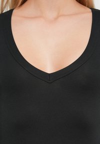 Μαύρο μπλουζάκι χωρίς μανίκια με βαθύ V-λαιμόκοψη, κατασκευασμένο από απαλό υλικό, εφαρμοστό και με ελάχιστες ραφές.