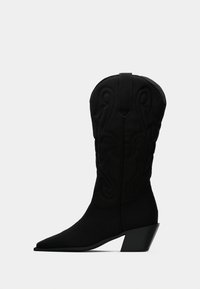 Μαύρο δυτικό μποτάκι μέτριου μήκους με μυτερή μύτη, διακοσμητικές ραφές, λουράκι για τράβηγμα και κεκλιμένο τακούνι με στιβάδες, πάνω σε απλό φόντο.
