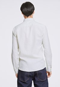 Ljusfärgad linnen skjorta med krage, långa ärmar och rak rygg. Bärs med mörka denimjeans, vilket visar en avslappnad stil.