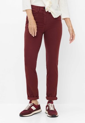 Frau trägt bordeauxfarbene, zulaufende Hose, die an den Bündchen hochgekrempelt ist, kombiniert mit passenden bordeauxroten und weißen Sneakern.
