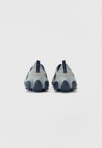 Grå og marineblå slip-on sko med en teksturert såle, rund form, og en stropp ved hælen for enkel påkledning.