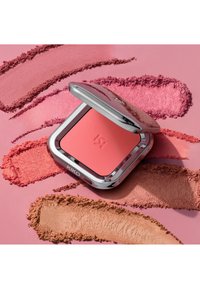 Roze blushcompact met een metalen zilverkleurige behuizing, met een gestructureerd oppervlak en een geperst logo. Eromheen roze en beige poedermonsters.