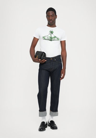 Weißes T-Shirt mit grünem Grafikmotiv, dunkelblaue Jeans mit aufgeschlagenen Säumen, schwarze Lederhandtasche und schwarze Loafers mit weißen Socken.