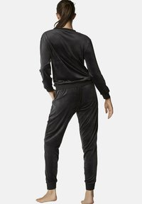 Zwart velours loungepakken set bestaande uit een top met lange mouwen en bijpassende broek. Zachte textuur, ontspannen pasvorm, met geribde manchetten en tailleband.