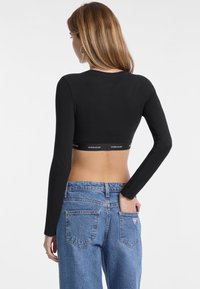 Top corto de manga larga negro con diseño ajustado y dobladillo con banda, combinado con jeans de mezclilla azul claro de cintura alta con bolsillos traseros.