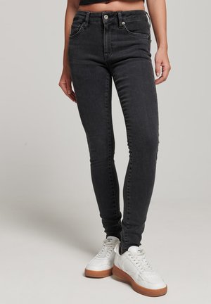 Zwarte hoog uitgesneden skinny jeans van denim, met vijf zakken, een ritssluiting en subtiele stikseldetails, gecombineerd met witte sneakers.