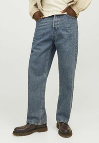 Heleh all-blue denim teksased on otse-jala disain, klassikaline viie taskuga stiil ja tagasihoidlikult pleekinud tekstuur. Kanda tumedate pruunide saapadega.