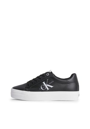 Zapatilla negra de caña baja con suela blanca de plataforma, cordones negros y el logo "CK Calvin Klein Jeans" en el lateral.