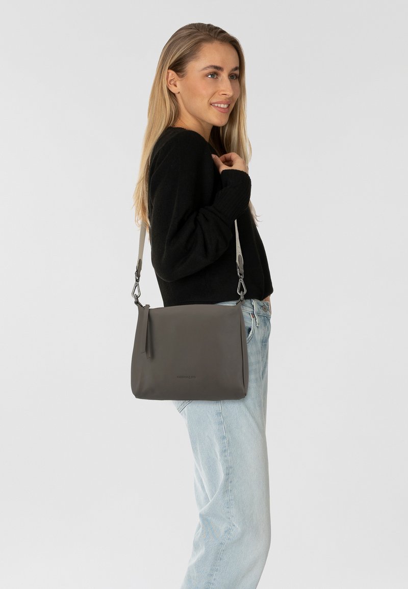 Bolso de hombro cruzado de piel gris con una textura suave, que cuenta con una larga correa ajustable, detalles de cremallera y un diseño minimalista.