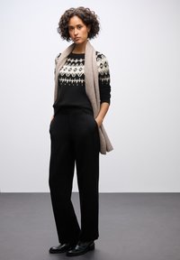 Czarny i biały sweter w wzory warstwowy z jasnobeżowym szalem, w połączeniu z czarnymi spodniami o kroju dopasowanym i czarnymi botkami za kostkę z złotymi akcentami.