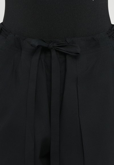 Black trousers featuring a tied waistband, pleated design, and side pockets, made from a lightweight fabric with a smooth texture.