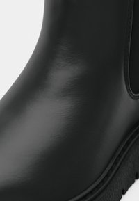 Μαύρη ελαστική μπότες ankle με γυαλιστερή φινίρισμα, υφασμάτινη πλευρική πάνελ και παχιά σόλα. Στρογγυλή μύτη με ανάγλυφες ραφές.