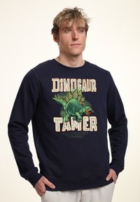 Sudadera de color azul marino hecha de algodón, con un gráfico de un dinosaurio y el texto "DOMADOR DE DINOSAURIOS" en letras coloridas y en negrita.