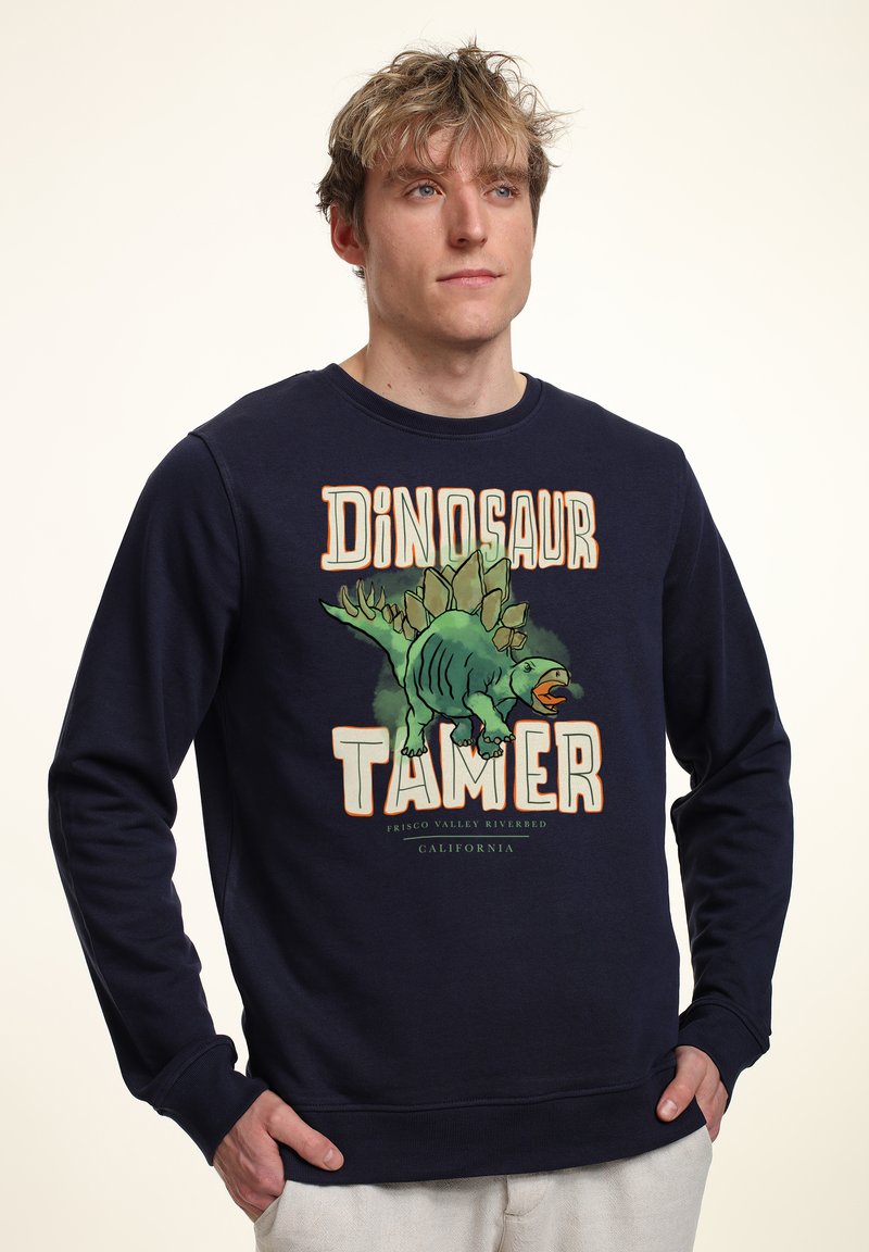 Sudadera de color azul marino hecha de algodón, con un gráfico de un dinosaurio y el texto "DOMADOR DE DINOSAURIOS" en letras coloridas y en negrita.