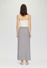 Grauer Maxirock mit elastischem Bund, aus leichtem Stoff. Getragen mit einem weißen, gerippten Tanktop und Sandalen mit Riemchen.