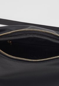 Musta nahkalaukku, jossa on kultainen vetoketju. Sisäosassa on sileä pinta ja lisävetoketjullinen tasku järjestämistä varten.