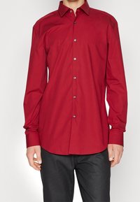 Rotes Hemd zum Knöpfen aus glattem Stoff, mit klassischem Kragen, langen Ärmeln und geradem Saum, sichtbare Knopfdetails.